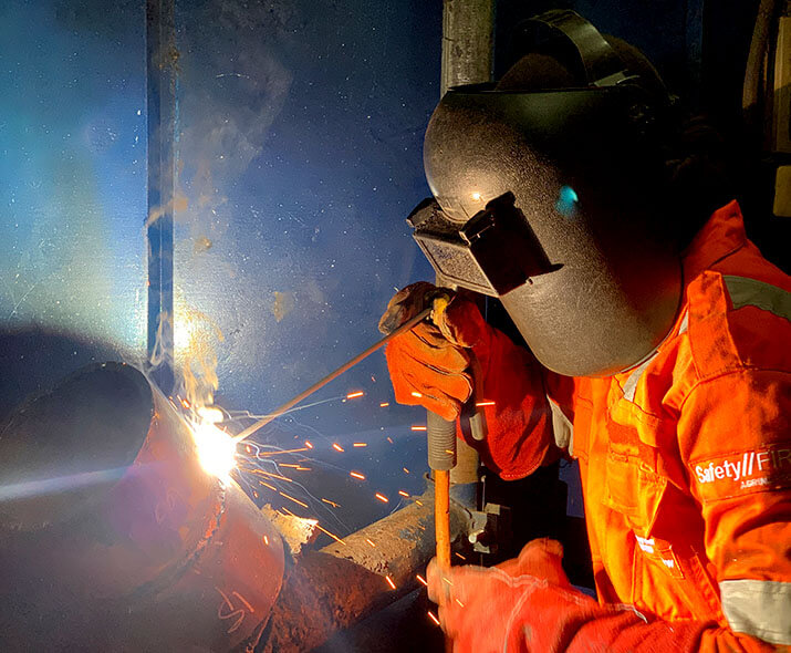 Welder in orange uniform and welding maslk