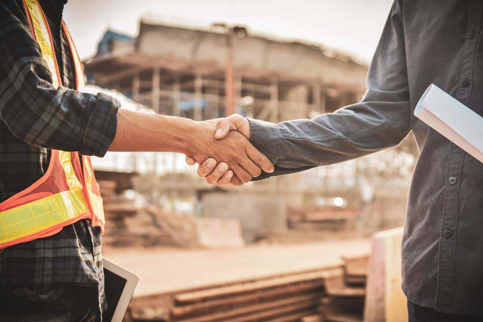 A construction worker and a foreman from a service provider company shaking hands in front of a workforce site