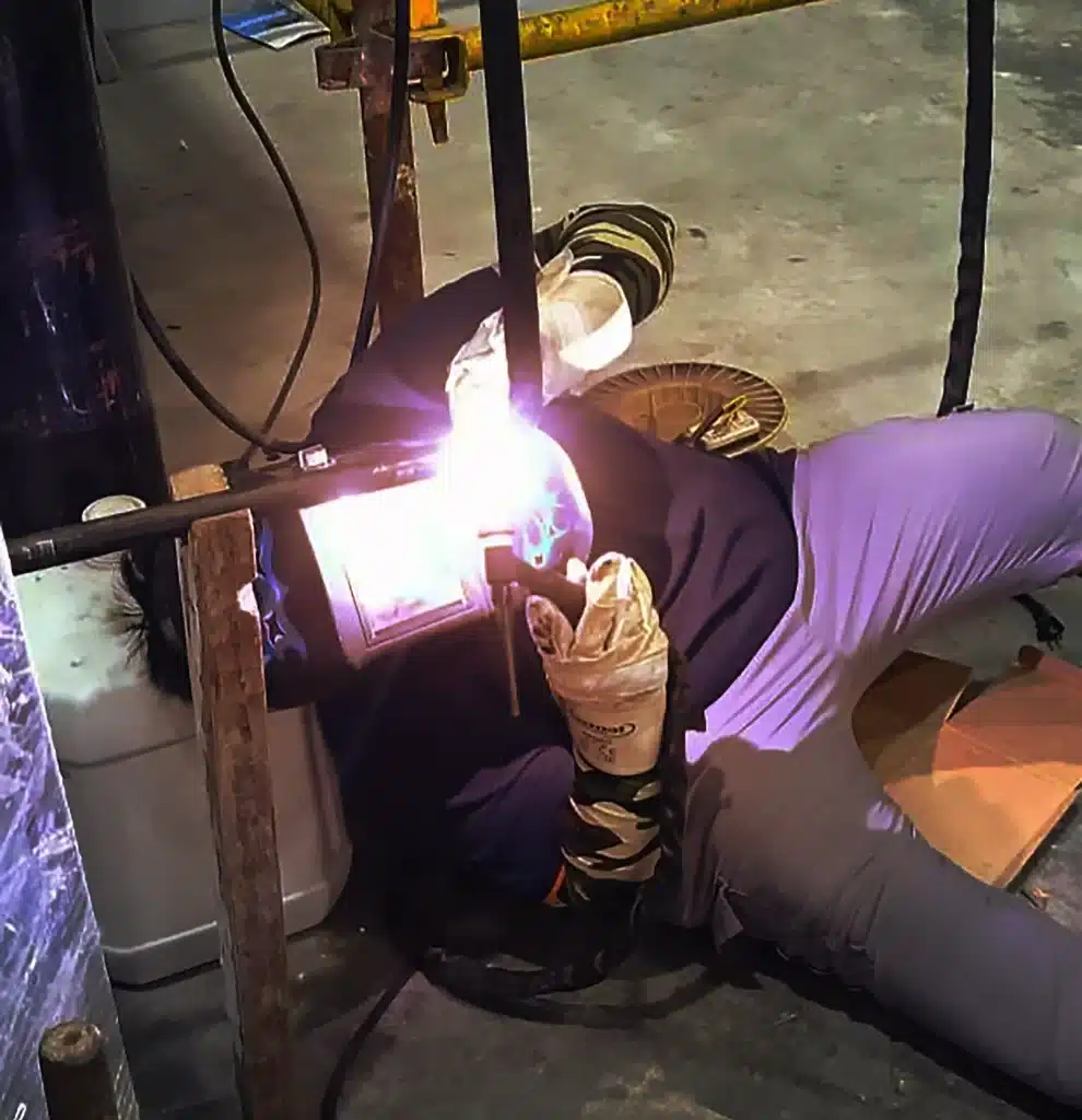 TOTC Welder, lying down while working with fabrication product.