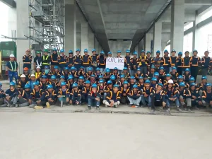 Construction crew in blue helmets and reflective vests posing under a concrete structure with scaffolding.