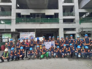 Construction crew in safety gear posing in front of a multi-story building under construction with TOTC Inc banners.