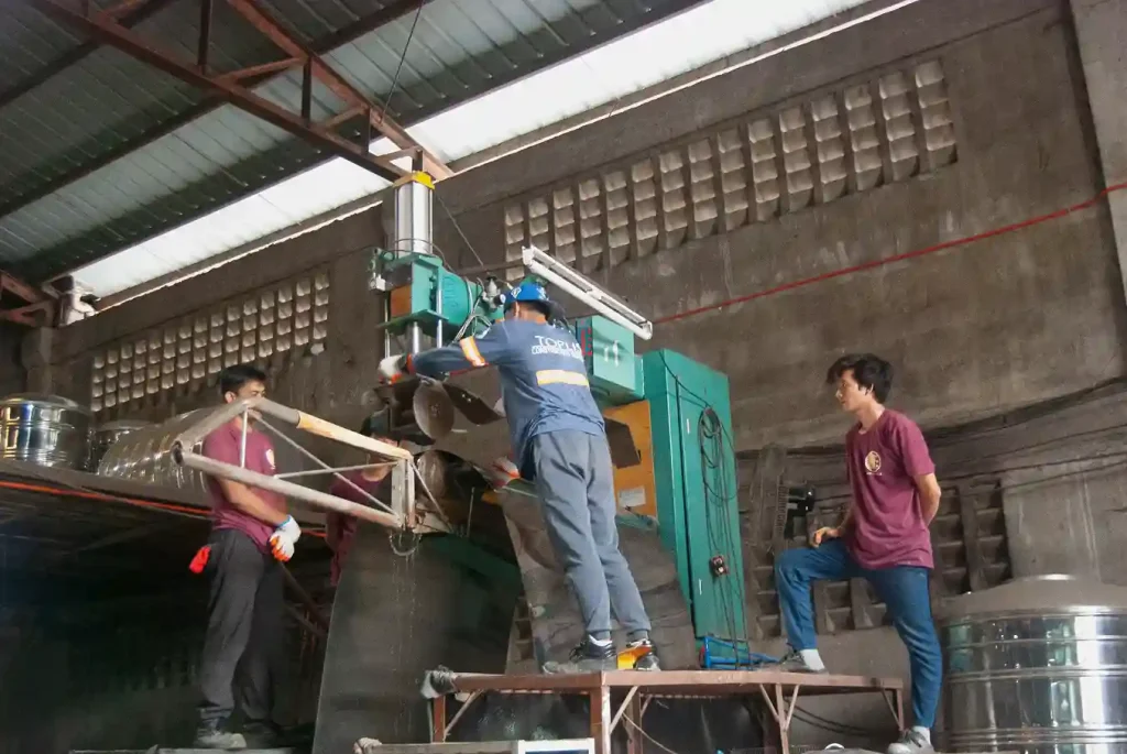 Four individuals operating a large green machine in an industrial facility with metal walls and equipment.