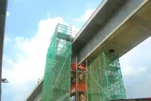 Elevated concrete bridge under construction with scaffolding, safety netting, and support pillars