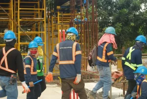A group of construction workers in safety gear preparing materials at an active site with scaffolding.